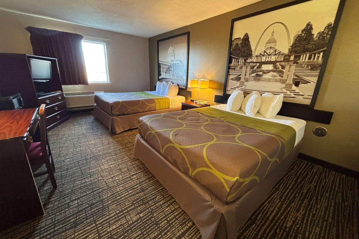 A hotel room with two beds, a desk, a TV, and a window.