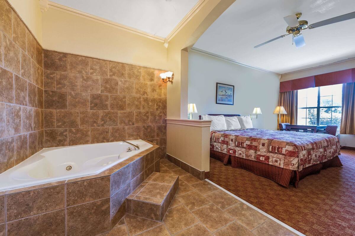 Une salle de bain avec une baignoire, une douche et des toilettes. On y trouve un lit recouvert d’une courtepointe et une fenêtre avec des rideaux.