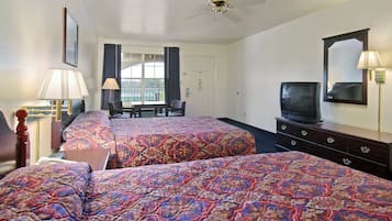 A hotel room with two beds, a television, a desk, and a window with curtains.