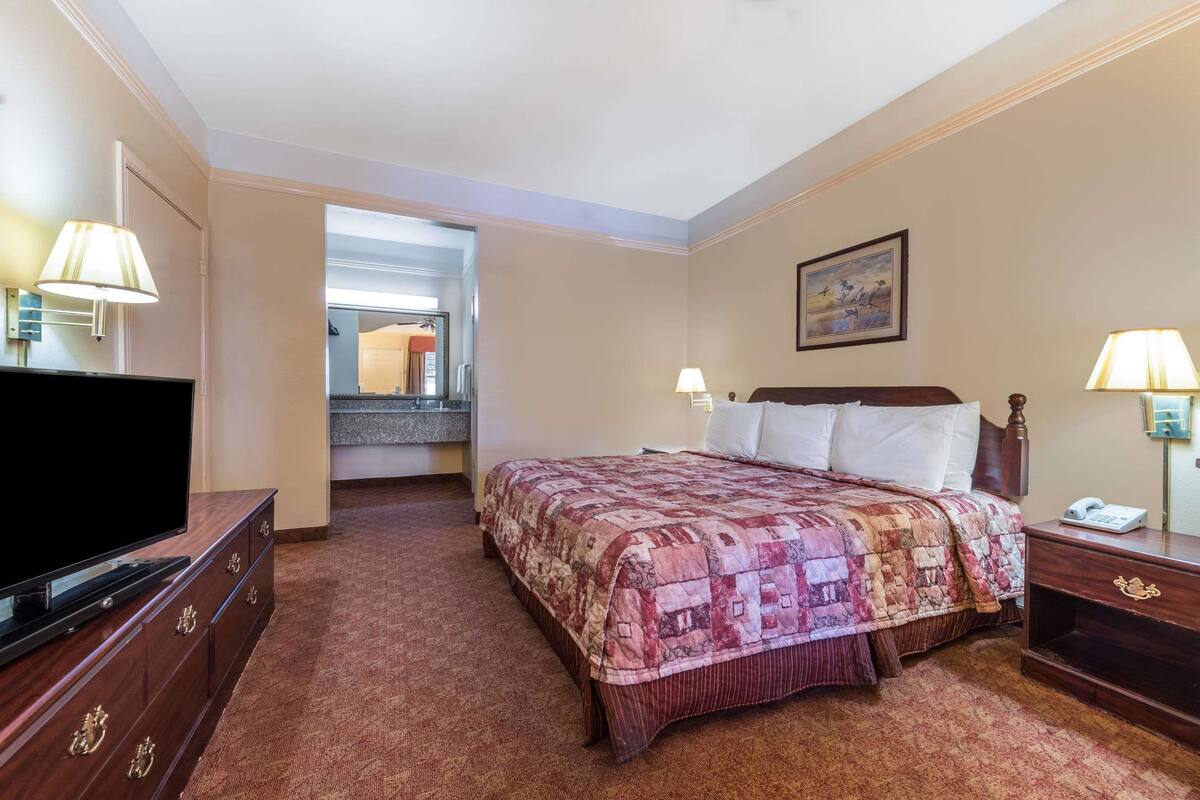 Une chambre d’hôtel avec un lit, une télévision, un bureau et une salle de bain, visibles à travers une porte ouverte.