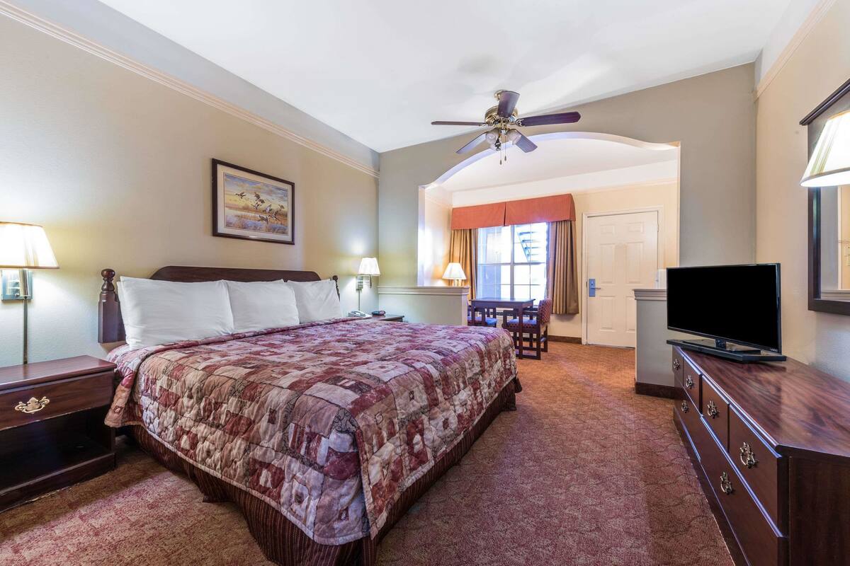 Une chambre d’hôtel avec un grand lit, un ventilateur de plafond, une télévision, un bureau avec une chaise et une porte donnant sur une autre pièce.