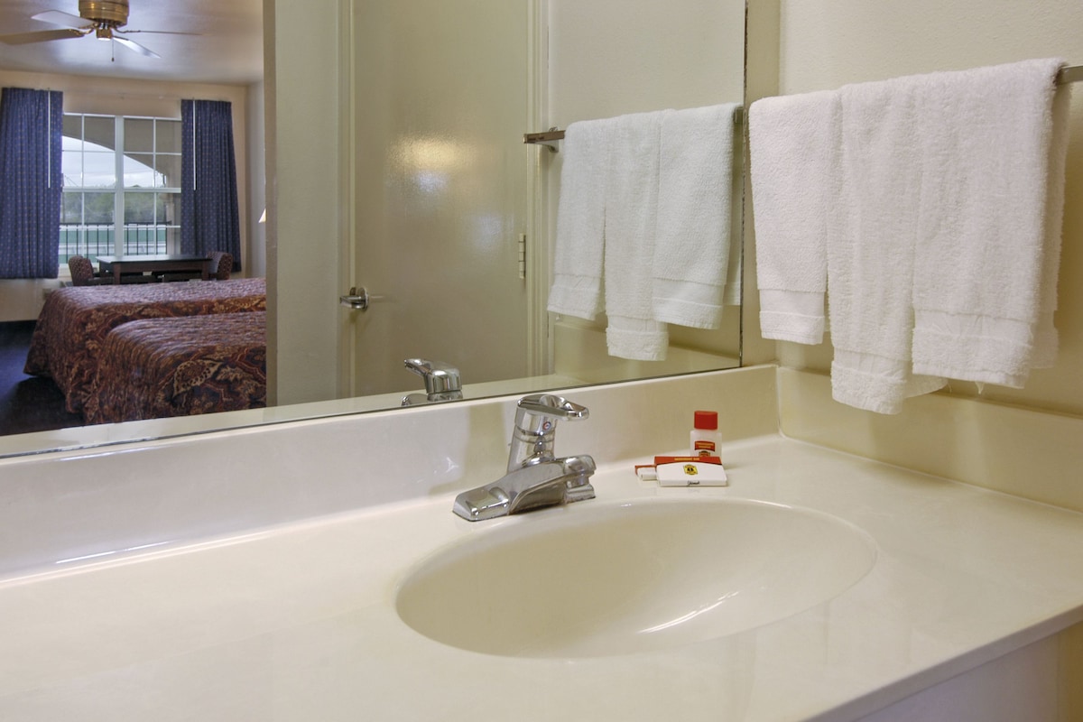 A hotel bathroom with a large mirror, white sink, and two towels hanging on the wall.