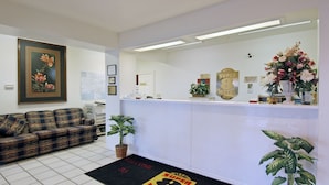 Un área de recepción con mostrador de registro, una obra de arte floral enmarco, un sofá y un felpudo de bienvenida.