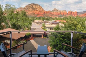 A view from a balcony overlooking a parking area with buildings and red rock formations in the background.