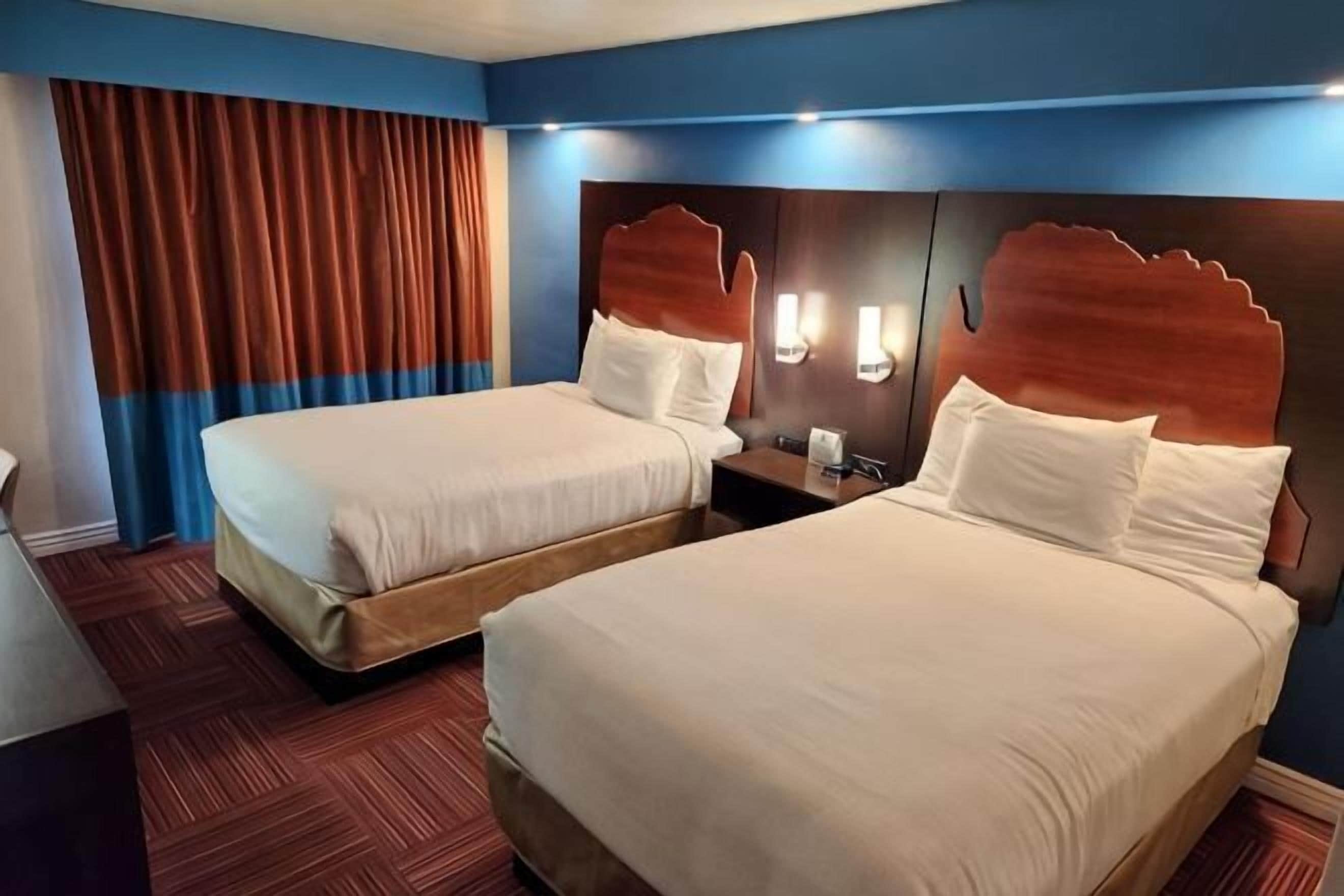 Ein Hotelzimmer mit zwei Betten, einem Holzkopfteil, einem Nachttisch und einem roten Teppichboden.