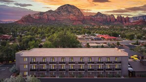 Un hotel de varios pisos con balcones, un estacionamiento y vistas a formaciones rocosas rojas al fondo.