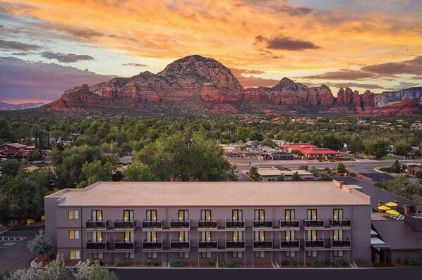 A multi-story hotel with balconies, a parking lot, and a view of red rock formations in the background.