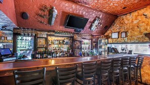 Un bar con pared de piedra, varias botellas de licor y un televisor colgado del techo.