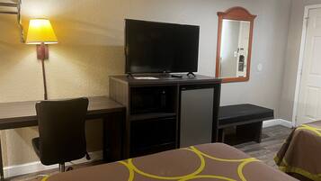 Een hotelkamer met een bed, een bureau met een televisie, een stoel en een lamp.