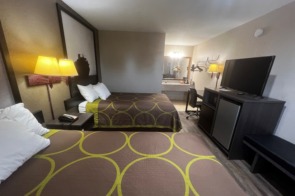 Et hotelværelse med seng, natbord, lampe, fjernsyn og et skrivebord med stol.