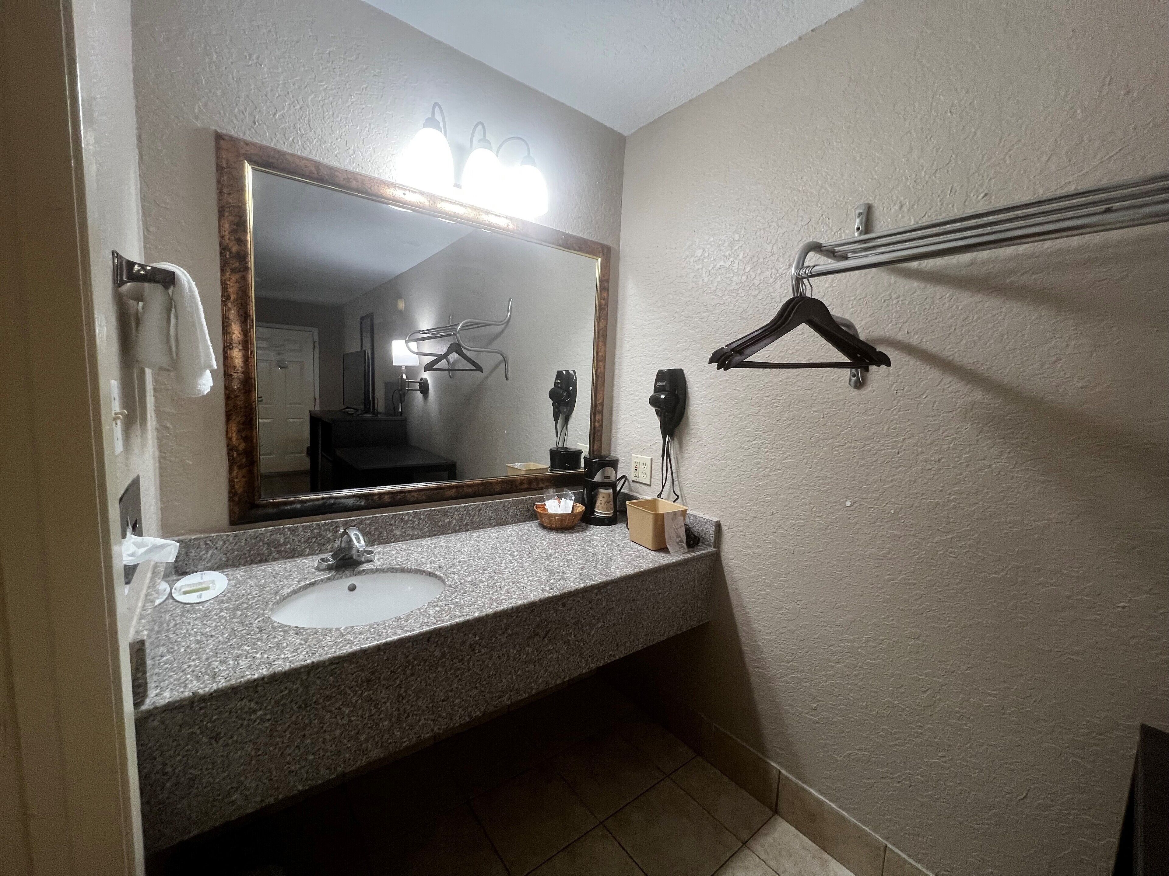 A bathroom with a granite countertop sink, a mirror with lights, a towel rack, and a hairdryer on the wall.