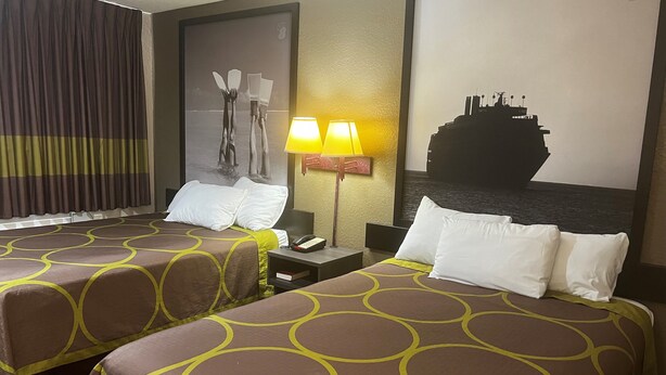 A hotel room with two beds, each with a brown and yellow patterned bedspread, a nightstand with a lamp, and a large framed picture on the wall. - Super 8 by Wyndham La Marque TX/Texas City Area (La Marque)