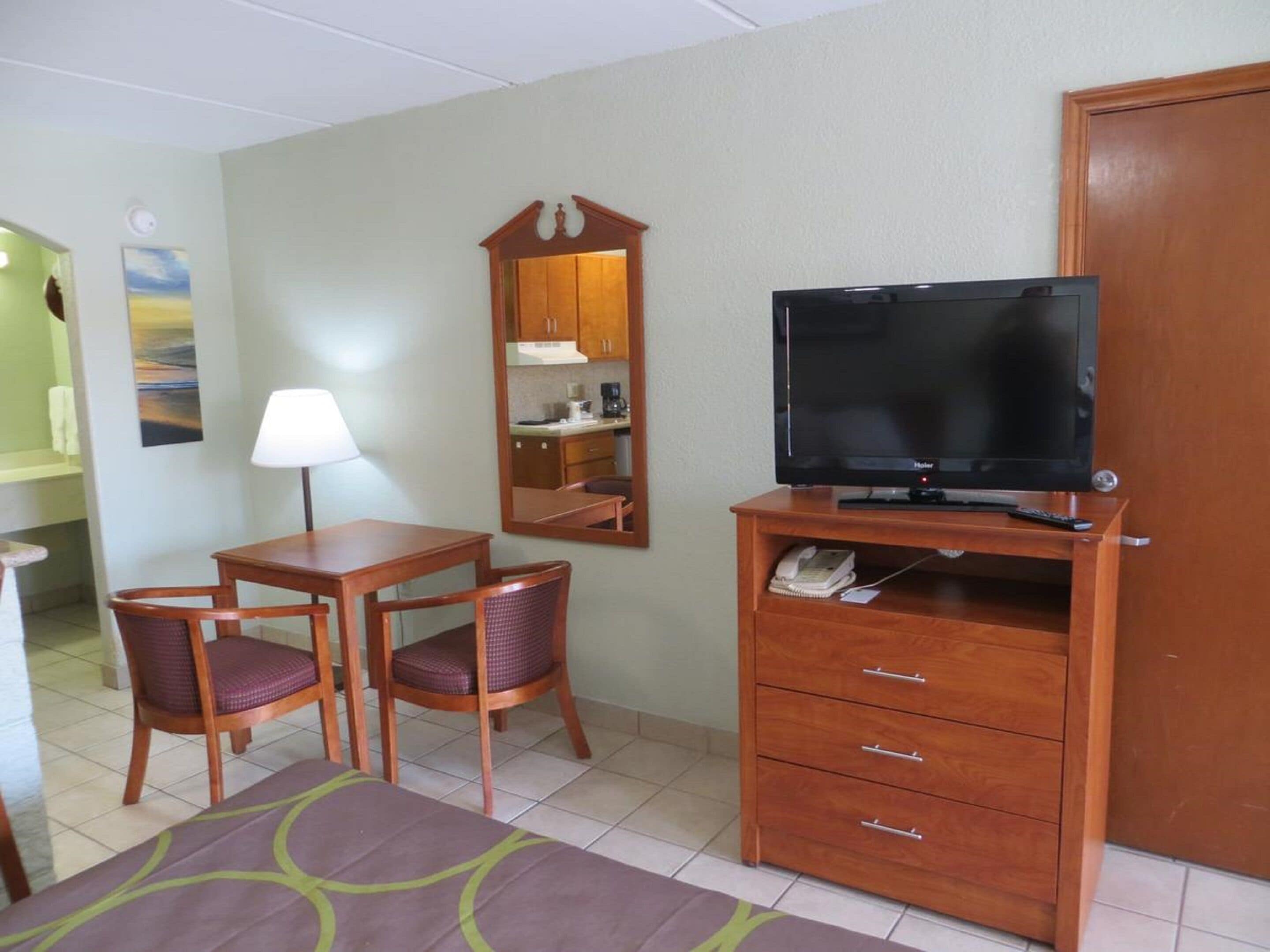Habitación de hotel con un escritorio de madera, dos sillas, un televisor sobre un mueble de madera, un espejo y un armario.