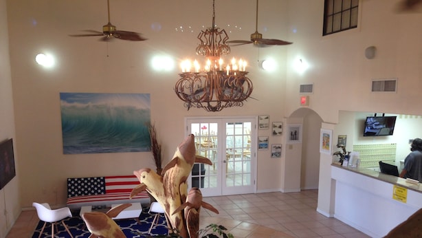 A lobby with a reception desk, a large American flag, a chandelier, ceiling fans, and a large painting of a wave. - Super 8 by Wyndham South Padre Island (South Padre Island)