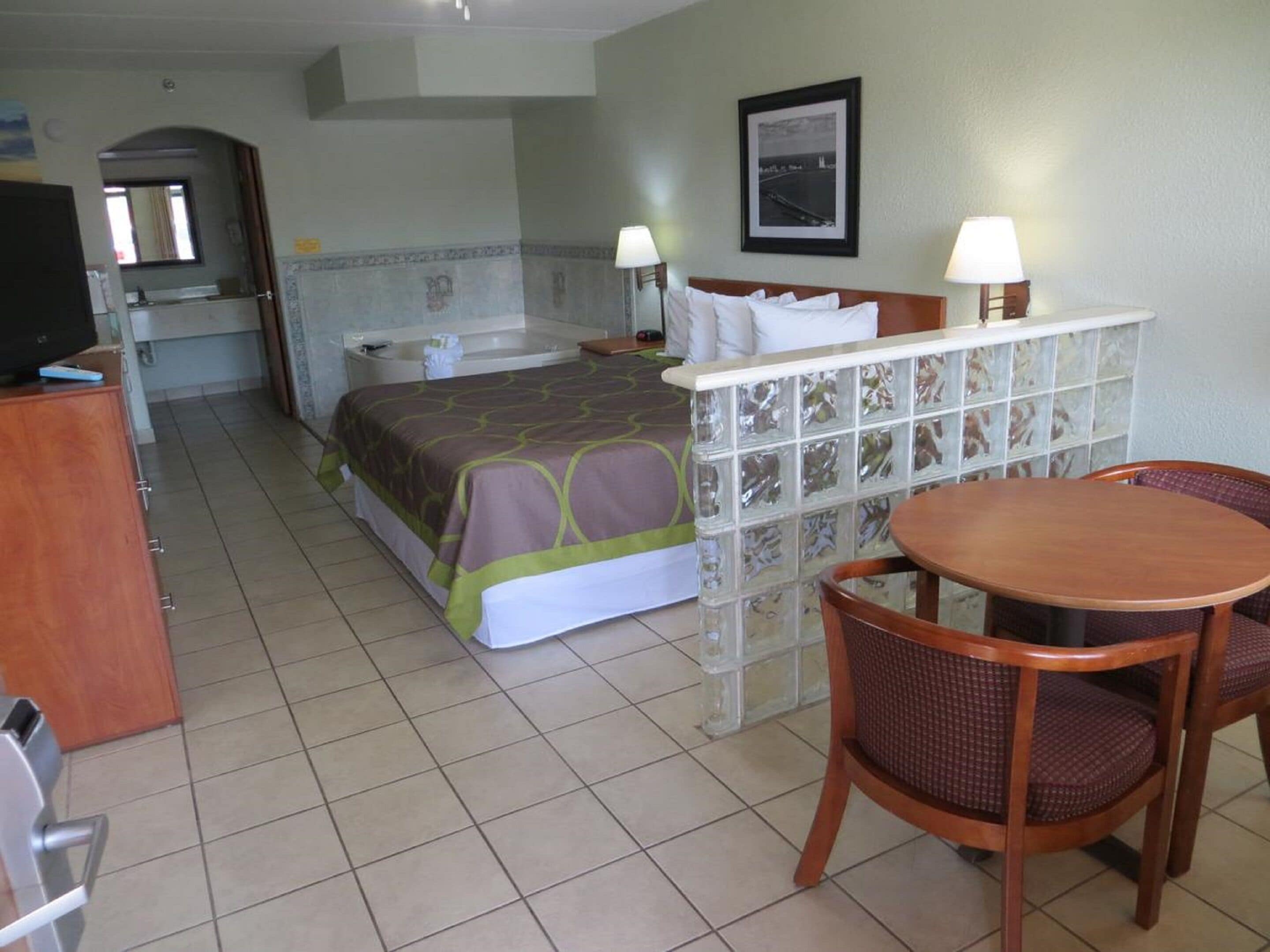 A hotel room with a bed, a desk, a chair, a table, a television, and a bathroom.