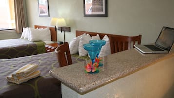 Habitación de hotel con dos camas, un escritorio con una computadora portátil, un florero con flores y una lámpara.