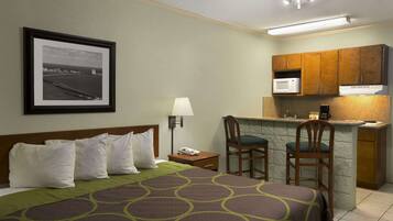 A hotel room with a bed, a desk with a chair, a microwave, and a small kitchen area.