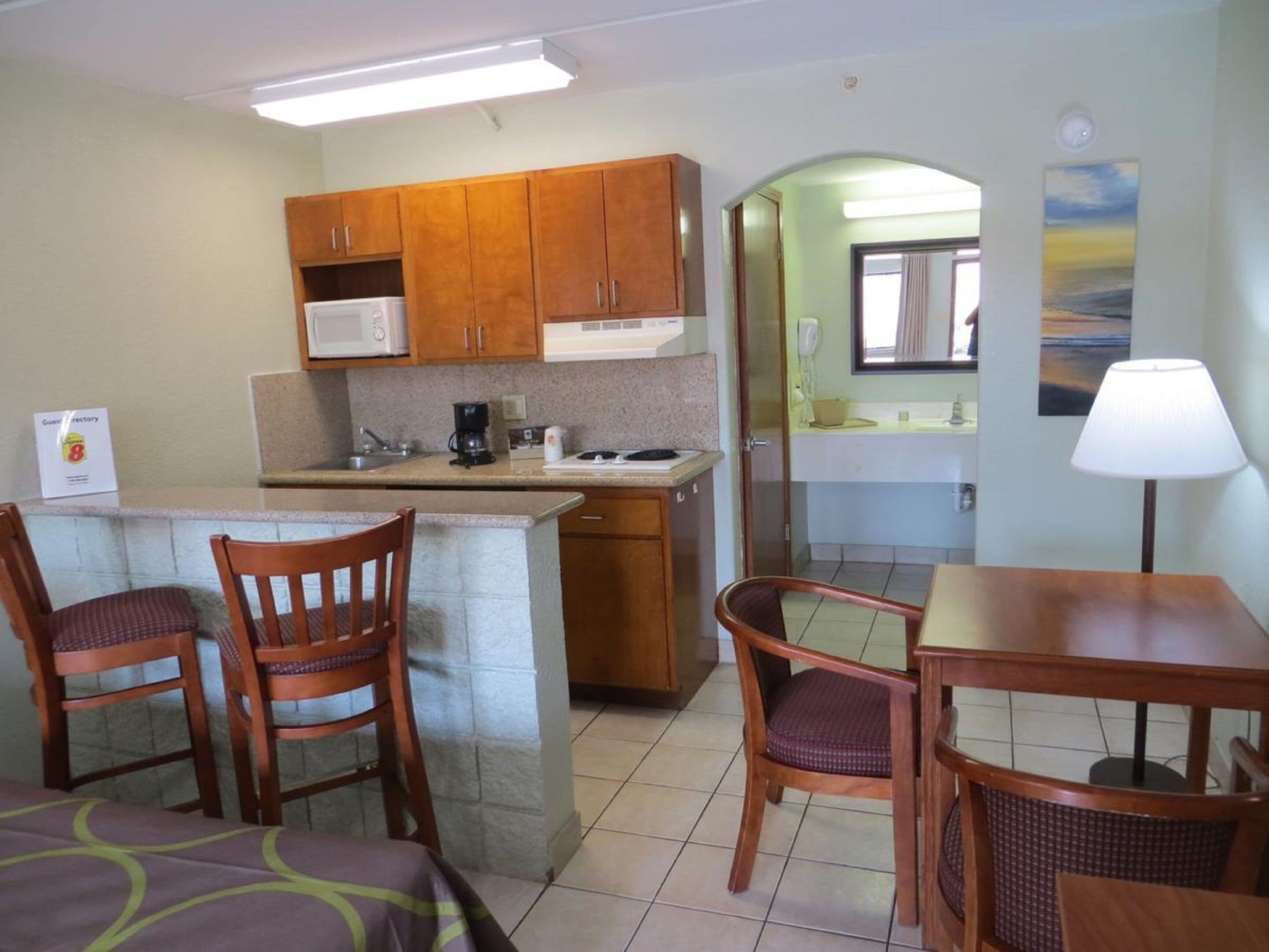 A compact kitchen with wooden cabinets, a microwave, and a coffee maker. There is a dining area with a table and chairs, and a small island with a sink.