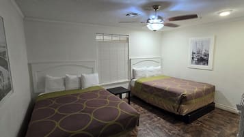 Habitación de hotel con dos camas individuales, ventilador de techo, ventana con persianas y un cuadro en la pared.