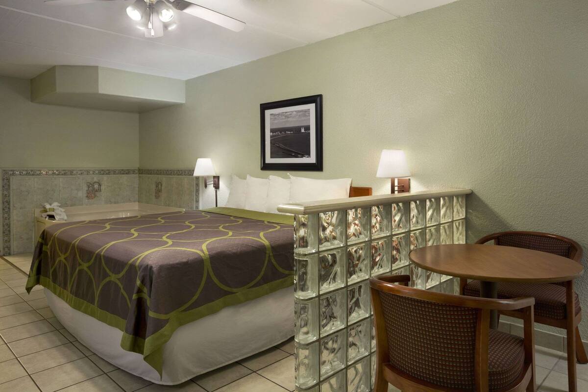 Une chambre d’hôtel avec un lit, une petite table, deux chaises, une table de chevet et un tableau accroché au mur.