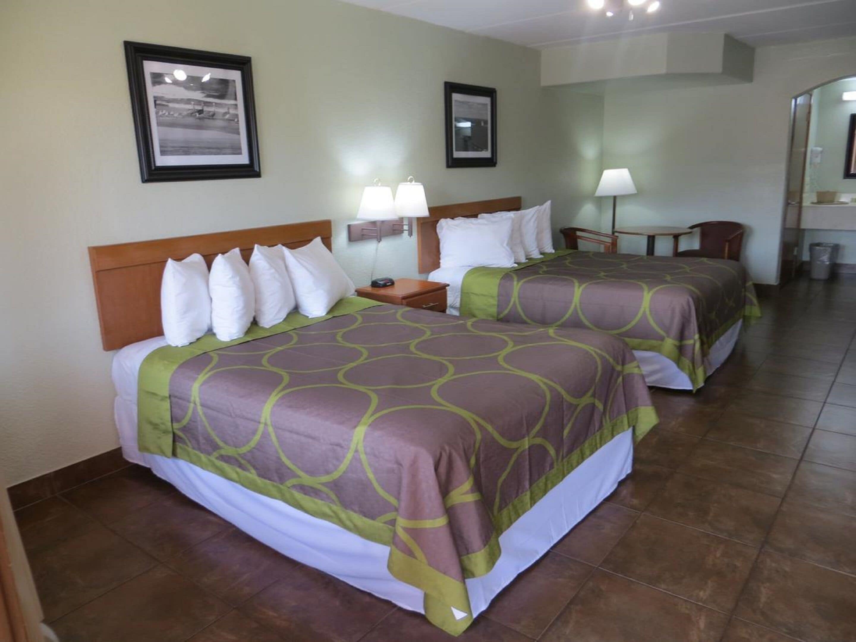 A hotel room with two beds, a nightstand, a desk, and a chair.