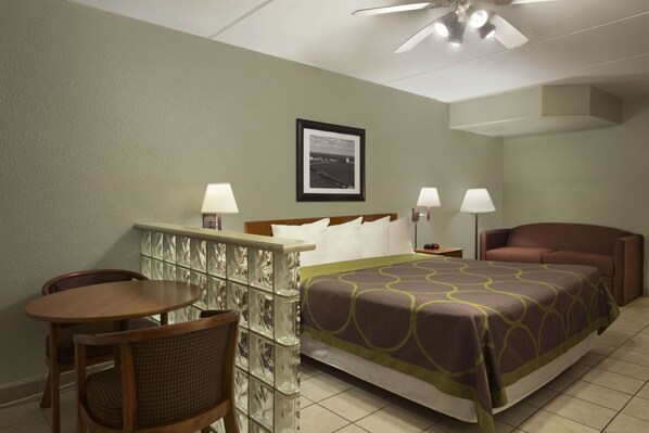 Habitación de hotel con cama, dos lámparas de noche, una silla, una mesita y un ventilador de techo.