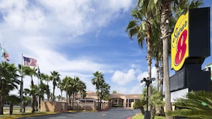 A hotel entrance with palm trees, an American flag, and a large sign for the hotel. - Super 8 by Wyndham South Padre Island (South Padre Island)