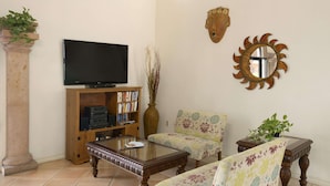 A living room with a television, bookshelf, two armchairs, a coffee table, and decorative items. - Super 8 by Wyndham South Padre Island (South Padre Island)