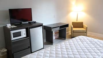 A hotel room with a bed, a desk with a television, a microwave, and a chair.