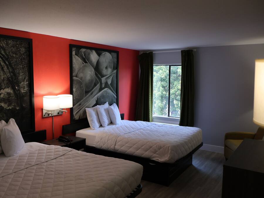 Habitación de hotel con dos camas, un cuadro abstracto grande en la pared, una ventana con cortinas y un escritorio con lámpara.