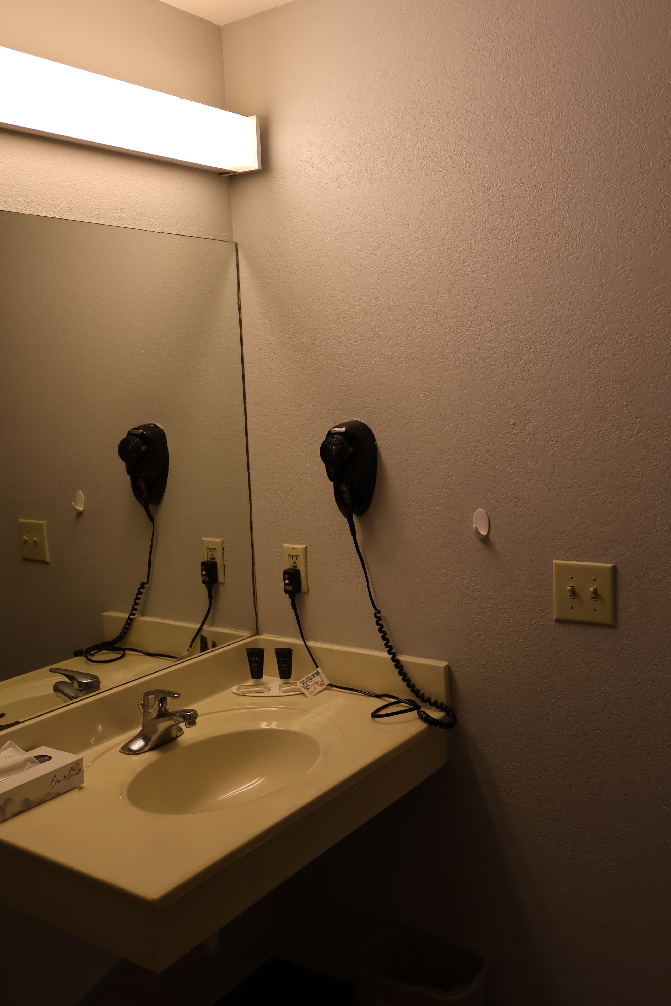 A bathroom with a sink, mirror, and hair dryer mounted on the wall.