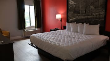 A hotel room with a large bed, a desk, a chair, a window with curtains, a wall-mounted lamp, and a painting.