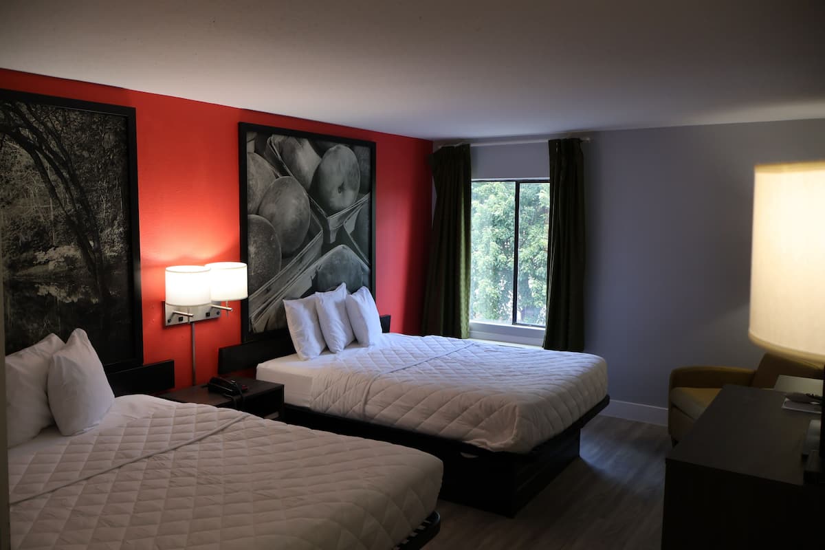 Habitación de hotel con dos camas, un cuadro abstracto grande en la pared, una ventana con cortinas y un escritorio con lámpara.