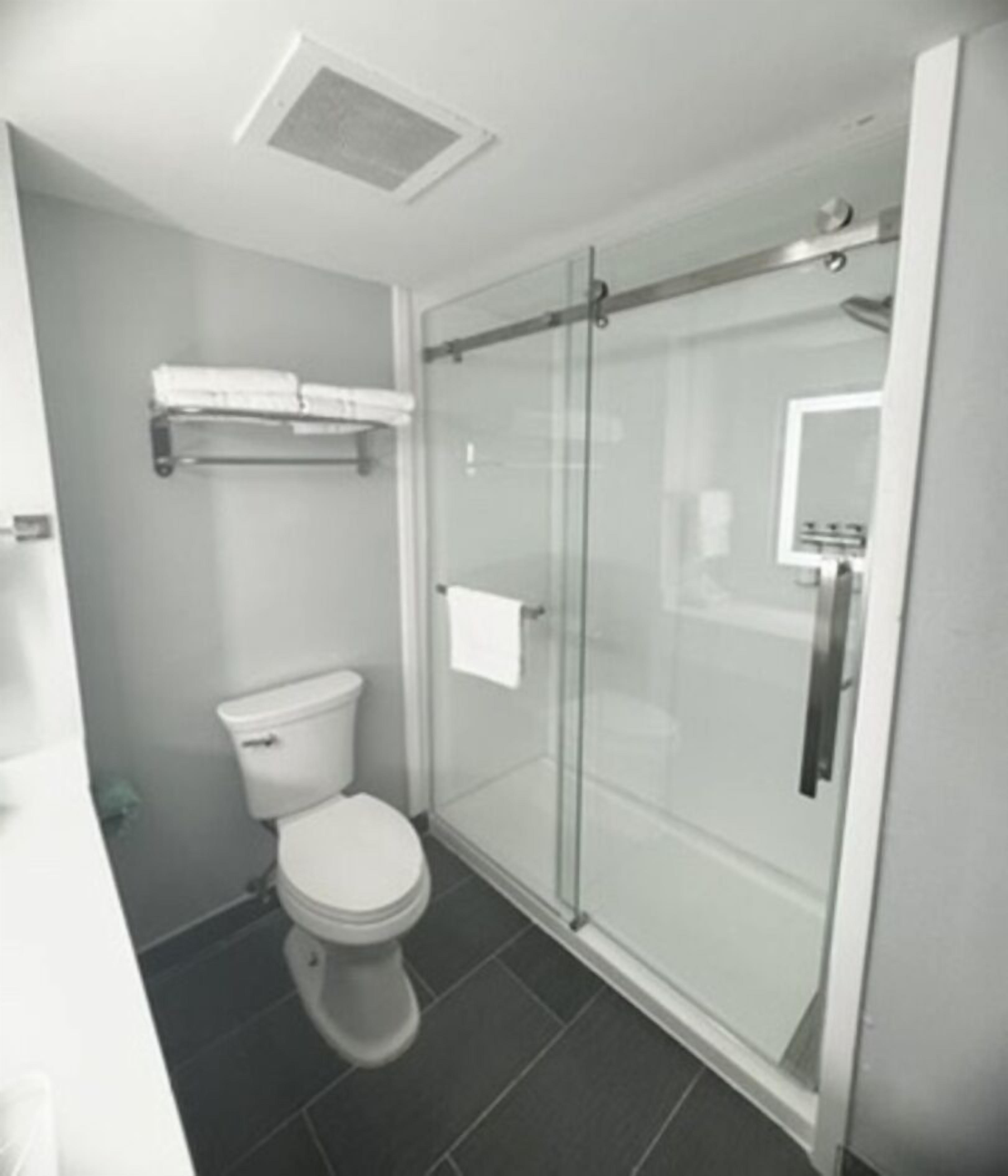 A small, modern bathroom with a toilet, a glass shower enclosure, and a towel rack.