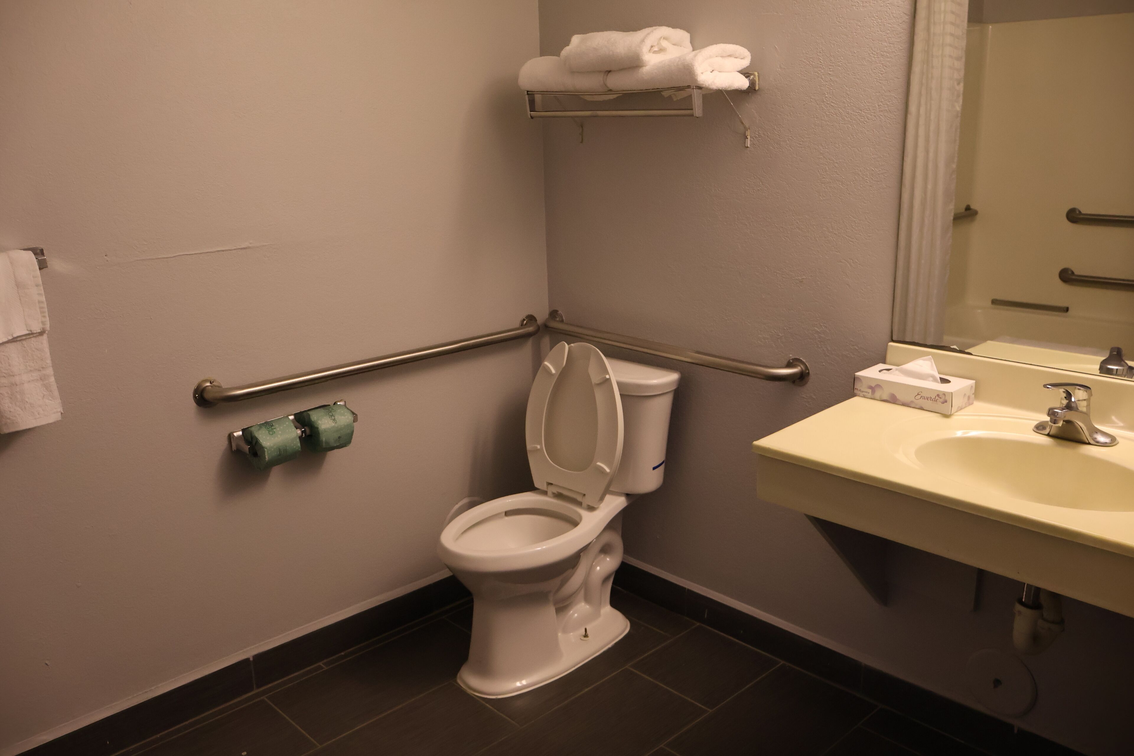 Un baño con inodoro, lavamanos, espejo y toallero.