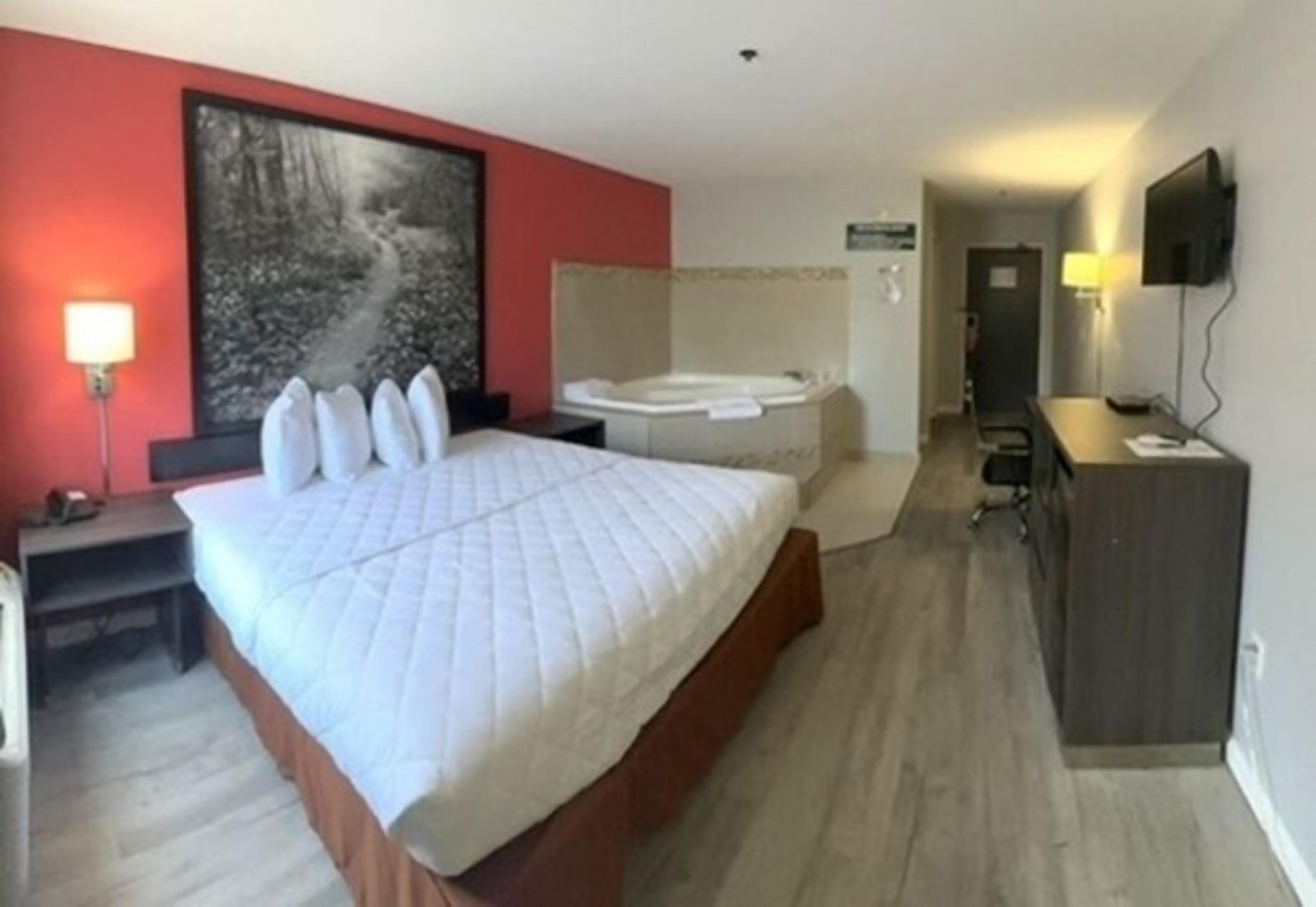 A hotel room with a large bed, a sitting area with a table and chairs, a TV, a desk, and a bathroom with a bathtub.