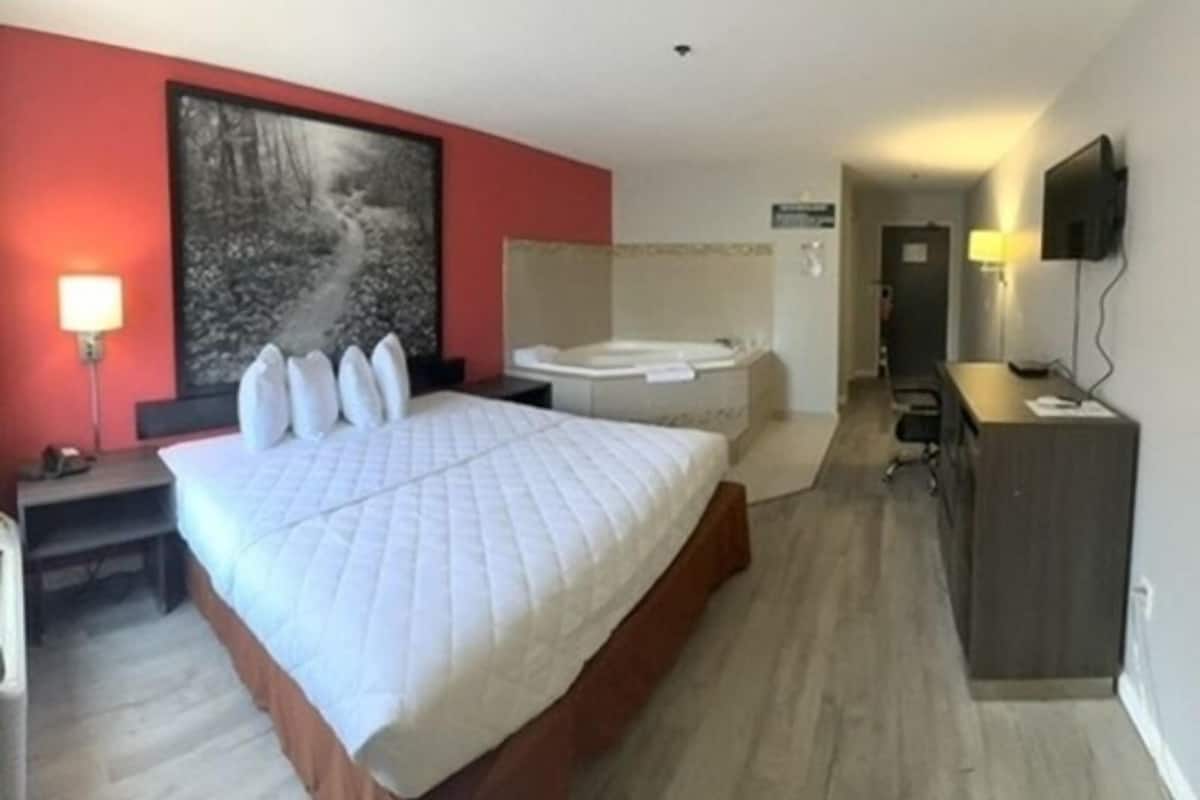 Habitación de hotel con una cama grande, una zona de estar con escritorio, televisor y un baño con bañera.
