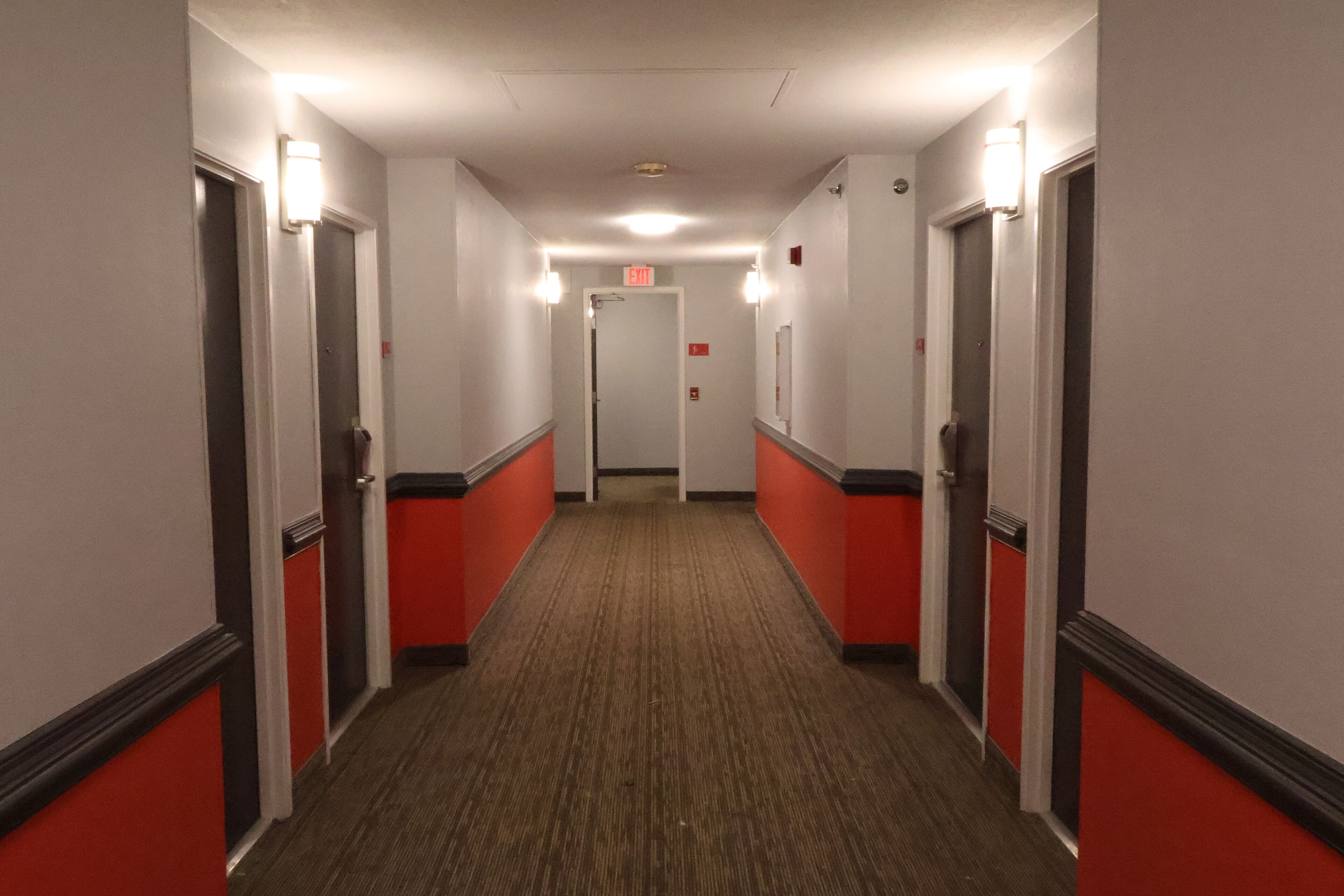 A hotel hallway with red and white walls, carpeted floors, and doors on both sides.