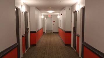 A hotel hallway with red and white walls, carpeted floors, and doors on both sides.