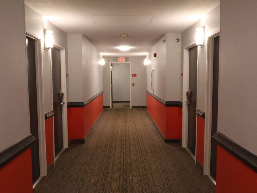 A hotel hallway with red and white walls, carpeted floors, and doors on both sides.