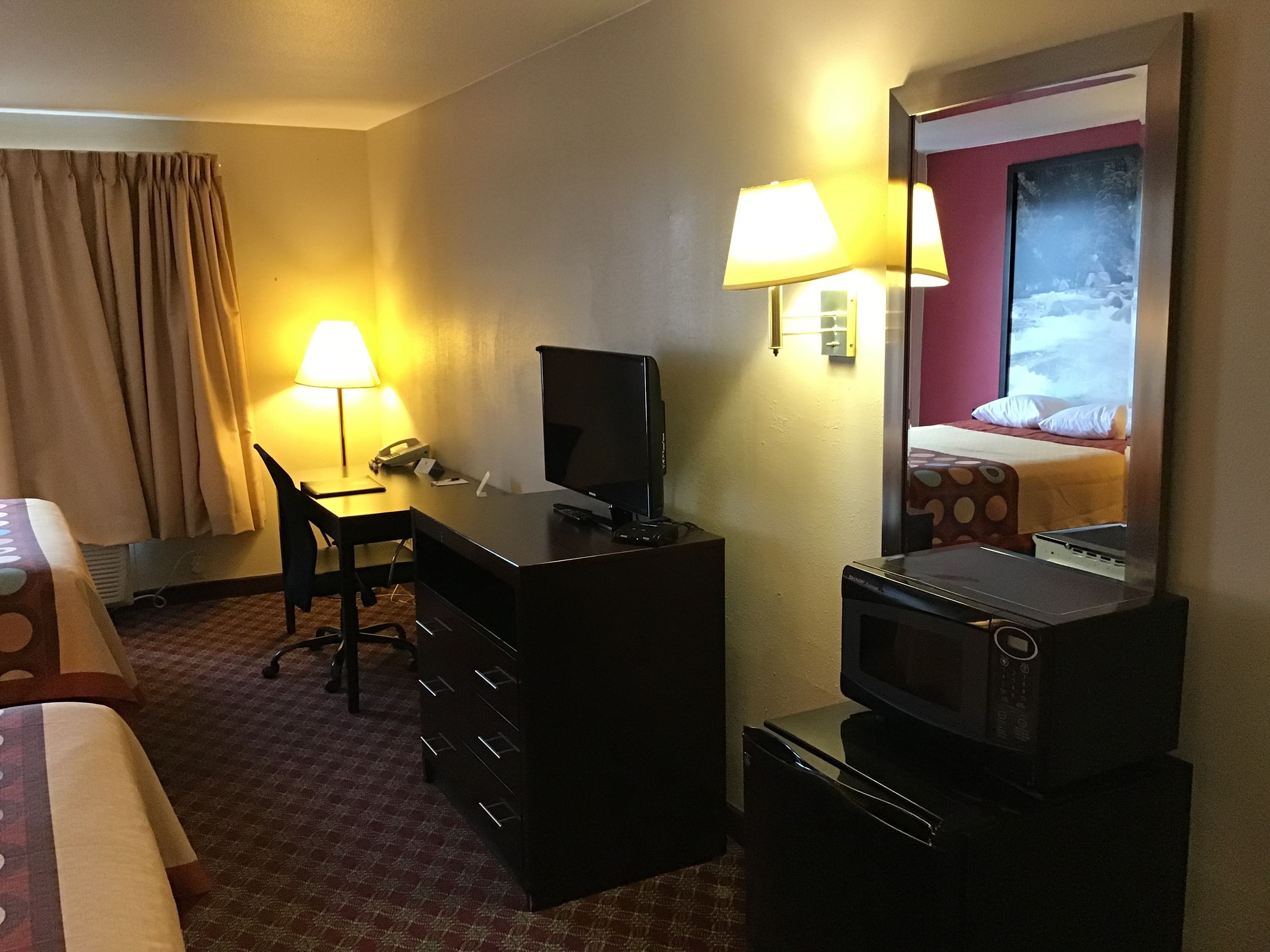 Habitación de hotel con escritorio, silla, televisor, microondas y cama con colcha estampada.