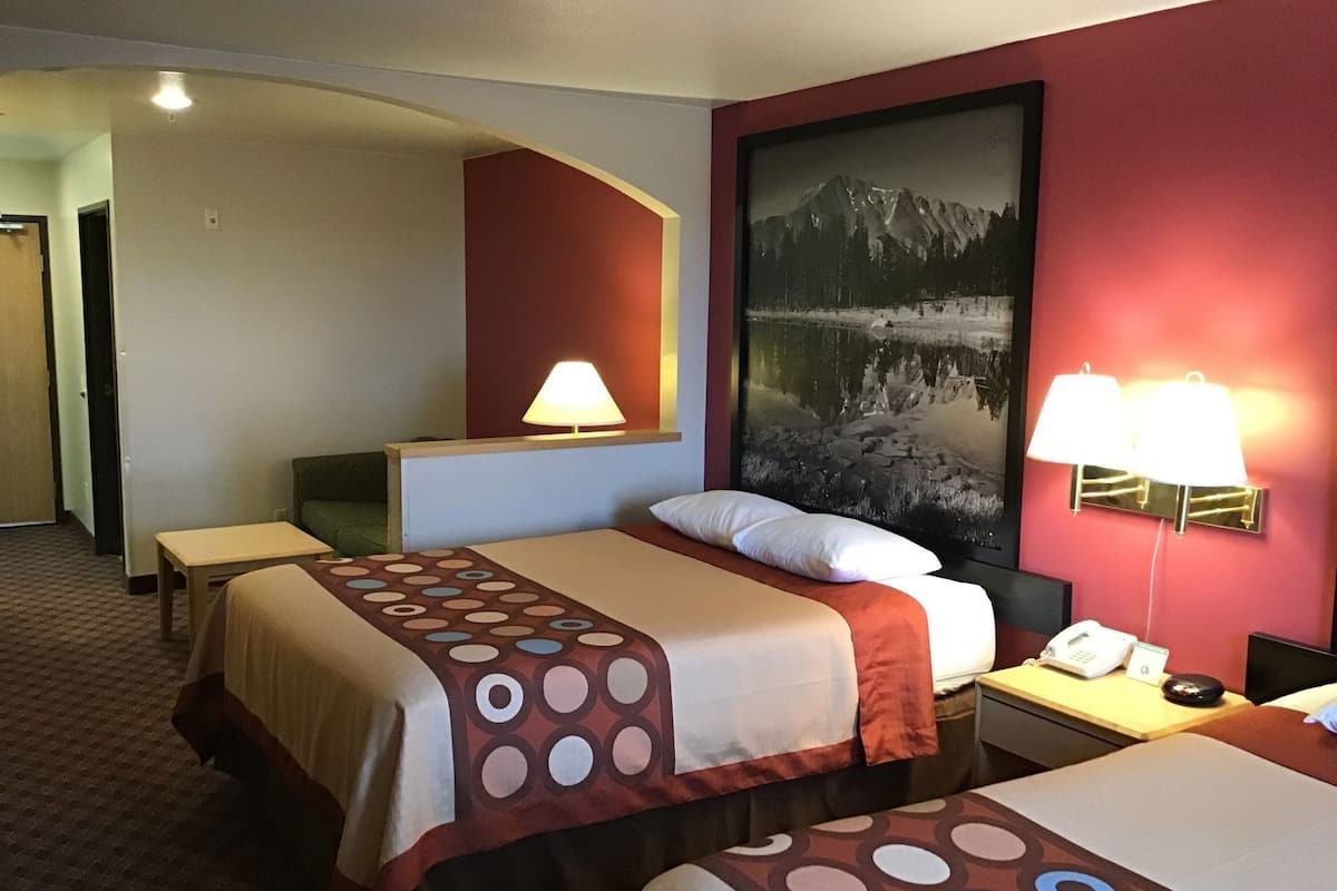 Hotelkamer met twee bedden, een bureau, een stoel, een lamp, een telefoon en een groot, ingelijst schilderij aan de muur.