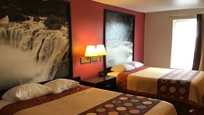 A hotel room with two beds, a large waterfall painting on the wall, a window with curtains, and a nightstand with a lamp.