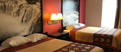 A hotel room with two beds, a large waterfall painting on the wall, a window with curtains, and a nightstand with a lamp.