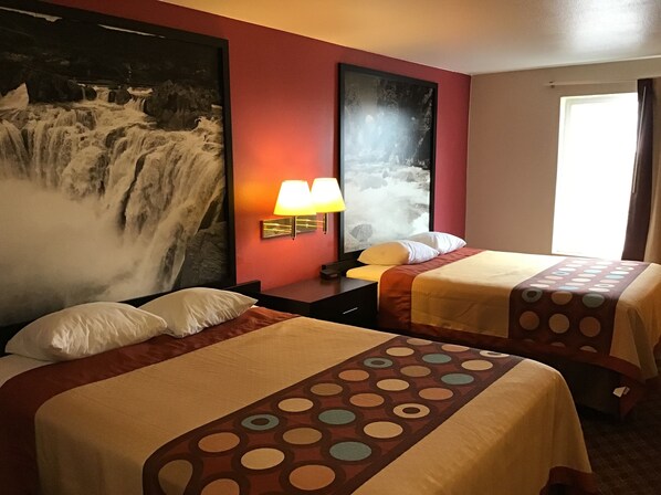 Habitación de hotel con dos camas, un cuadro grande de una cascada en la pared, una ventana con cortinas y una mesita de noche con una lámpara.