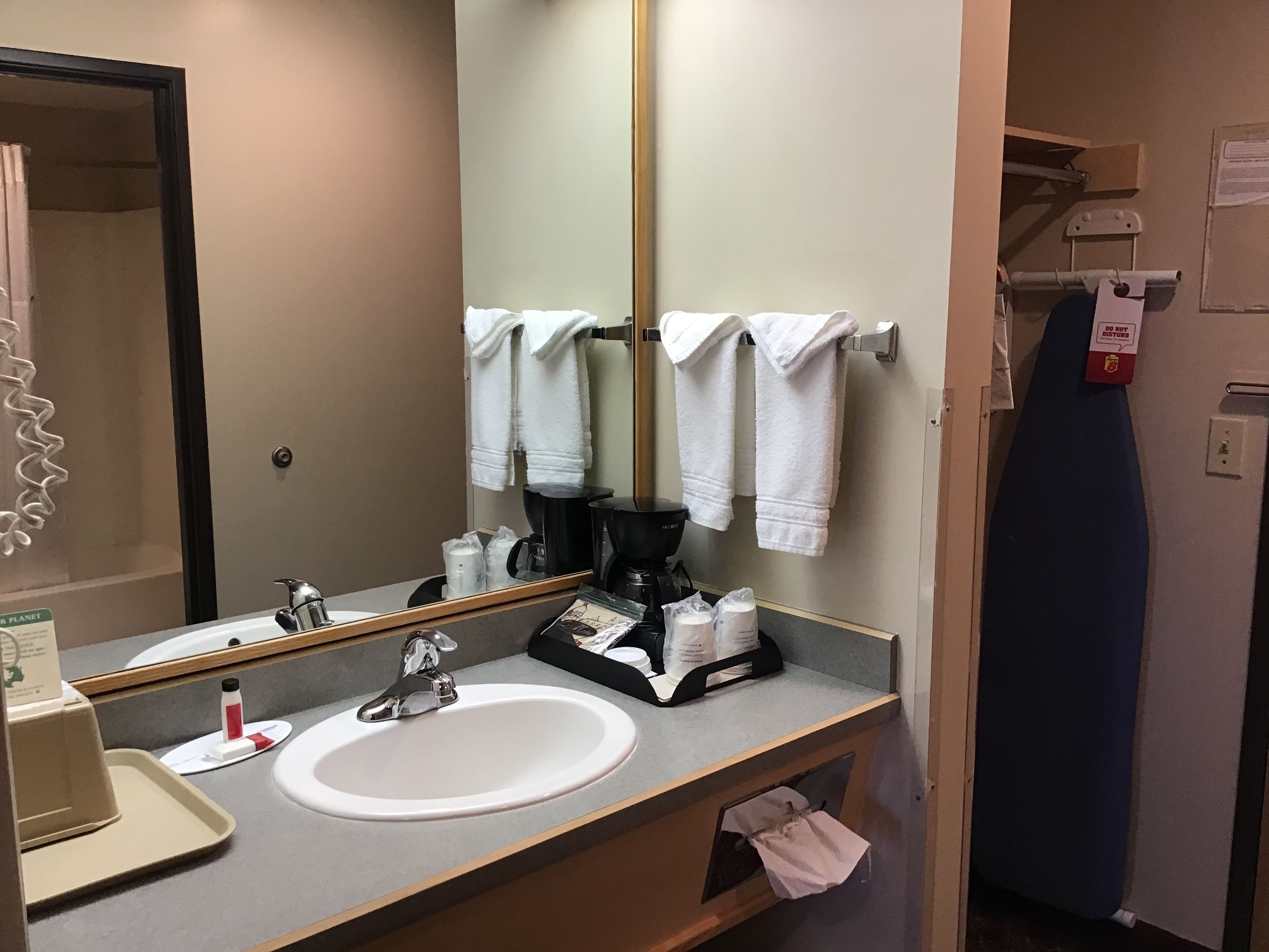 Un baño de hotel con lavamanos, espejo, toallero y cafetera.