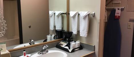 A hotel bathroom with a sink, mirror, towel rack, and a coffee machine.