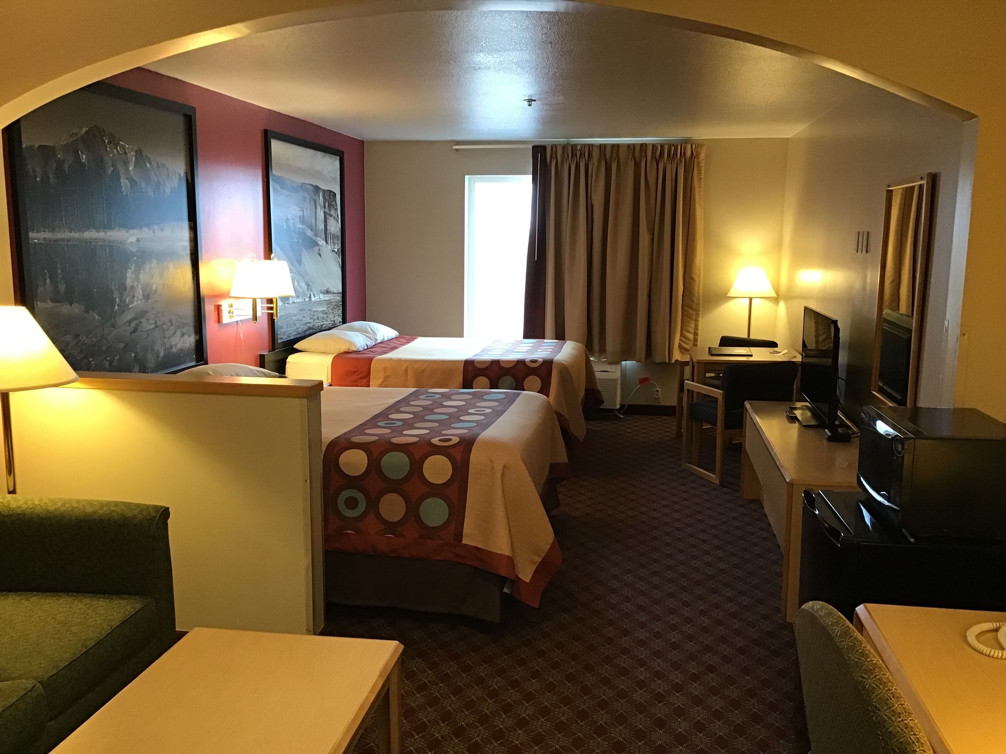A hotel room with two beds, a desk, a TV, and a painting on the wall.