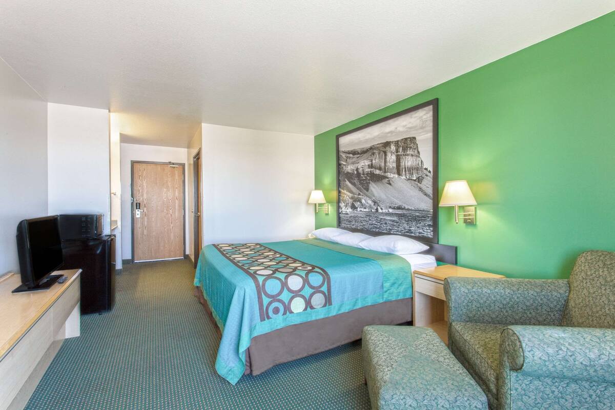 Een hotelkamer met een bed, twee bedlampen, een bureau, een televisie en een stoel.