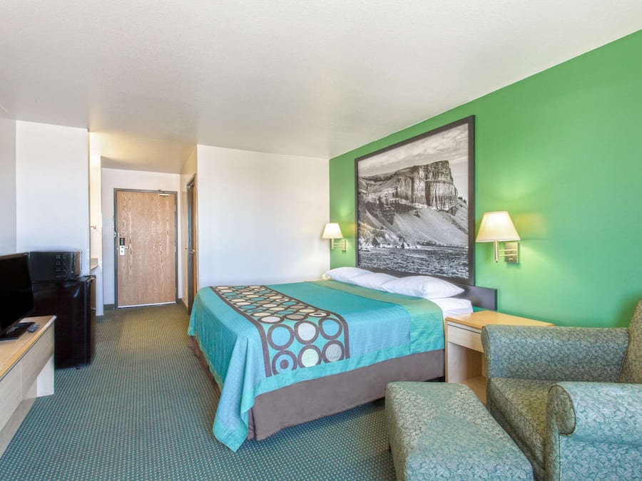 A hotel room with a bed, two bedside lamps, a desk, a television, and a chair.